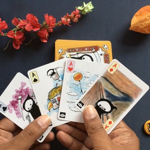 Puede incluir: Cuatro cartas de juego con una ilustraci&oacute;n en blanco y negro de un segador en cada carta. Las cartas son el As de Picas, el As de Corazones, el As de Diamantes y el As de Tr&eacute;boles. Las cartas se sostienen en una mano.