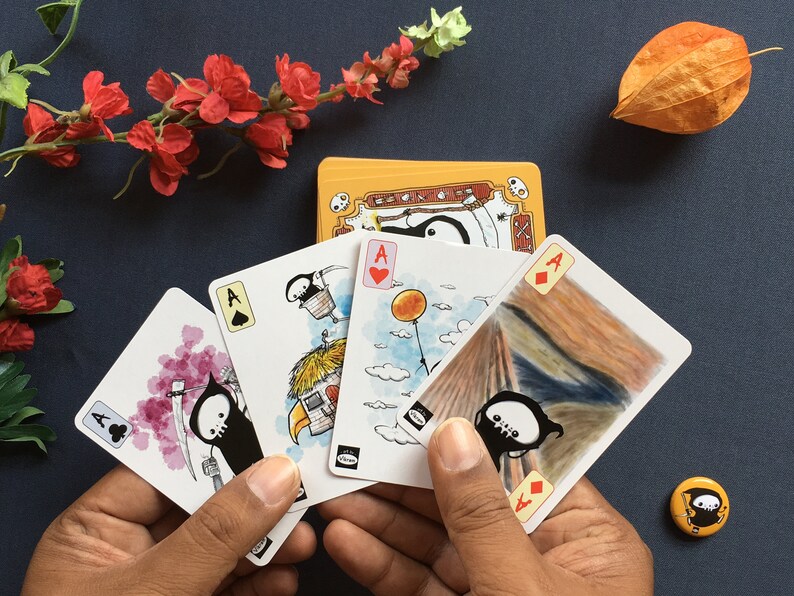 Puede incluir: Cuatro cartas de juego con una ilustraci&oacute;n en blanco y negro de un segador en cada carta. Las cartas son el As de Picas, el As de Corazones, el As de Diamantes y el As de Tr&eacute;boles. Las cartas se sostienen en una mano.