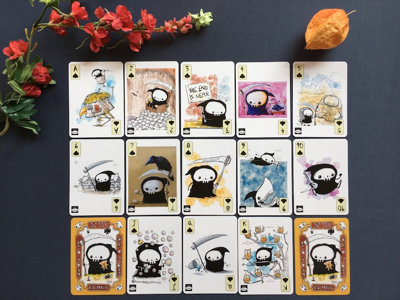 Puede incluir: Una baraja de cartas de juego con una caricatura de la Muerte en varias situaciones humor&iacute;sticas. Las cartas son del tama&ntilde;o est&aacute;ndar de las cartas de juego y presentan los palos est&aacute;ndar de picas, corazones, diamantes y tr&eacute;boles. Las cartas est&aacute;n impresas en cartulina blanca con tinta negra.