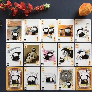 Puede incluir: Una baraja de cartas completa con un personaje de la Muerte, oscuro y de dibujos animados, en cada carta. Las cartas son blancas con bordes negros y s&iacute;mbolos de diamantes rojos. Las cartas est&aacute;n ordenadas de As a Rey.