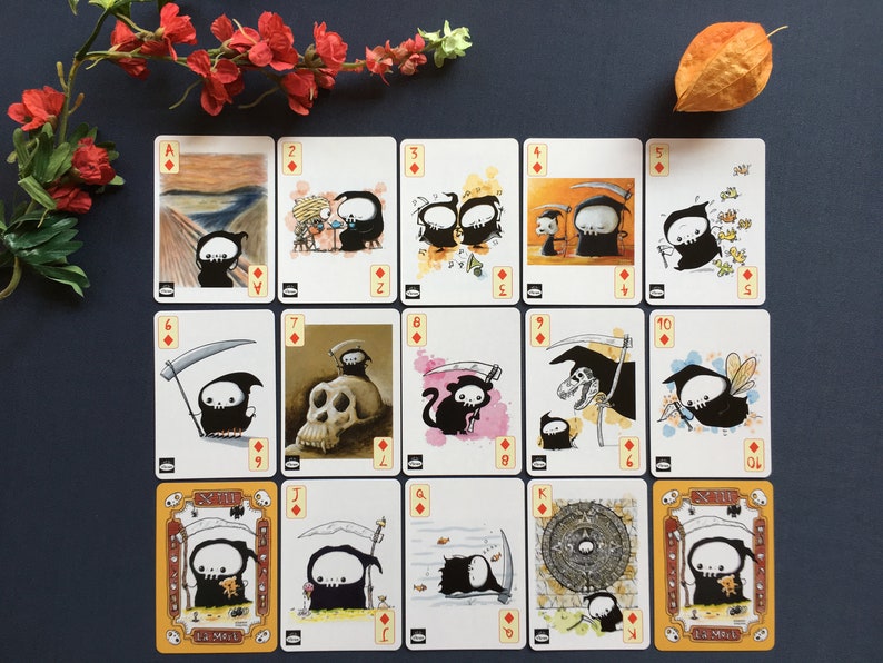 Puede incluir: Una baraja de cartas completa con un personaje de la Muerte, oscuro y de dibujos animados, en cada carta. Las cartas son blancas con bordes negros y s&iacute;mbolos de diamantes rojos. Las cartas est&aacute;n ordenadas de As a Rey.