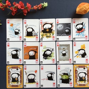 Puede incluir: Una baraja de cartas de juego con una caricatura de la Muerte con una guada&ntilde;a. Las cartas est&aacute;n numeradas del 1 al 10, J, Q, K y A. Las cartas son del palo de corazones.