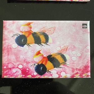 Könnte beinhalten: Zwei Comic-Elfen mit roten Mützen reiten auf Hummeln mit schwarzen und gelben Streifen. Die Hummeln fliegen vor einem rosa Hintergrund mit weißen Blasen.