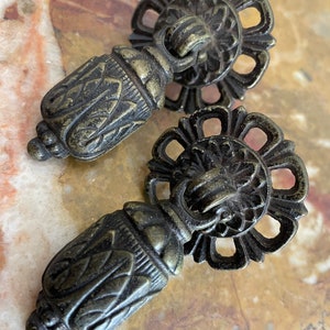 May include: Two antique brass cabinet knobs with ornate floral designs. The knobs have a round base with a decorative ring and a small, round handle.