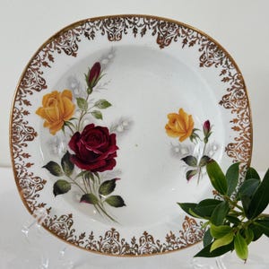 May include: A white ceramic bowl with a gold rim and floral design. The bowl features red, yellow, and white roses with green leaves. The bowl is ideal for serving soup, salad, or fruit.