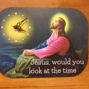 A rectangular novelty clock with a picture of Jesus praying to the heavens.  The clock face is to one side.  Jesus is not looking at it.  Text on the clock face says Jesus would you look at the time.