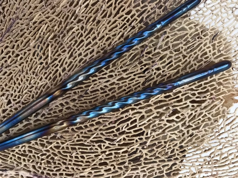 May include: Two blue and silver twisted metal chopsticks on a brown textured surface.