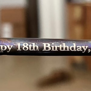 May include: A close-up of a metal rod with the inscription "Happy 18th Birthday, Dylan" engraved on it.
