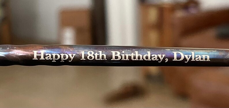 May include: A close-up of a metal rod with the inscription "Happy 18th Birthday, Dylan" engraved on it.