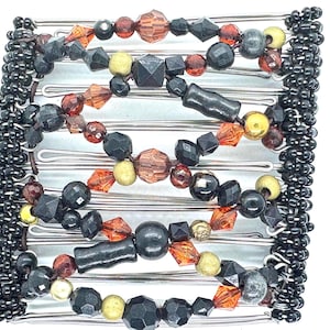 May include: A silver hair comb with black, gold, and red beads. The comb is made of metal and has a series of teeth on one side. The beads are arranged in a decorative pattern.