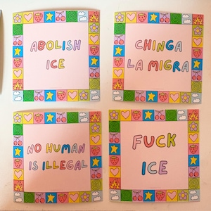 Op de afbeelding: Vier vierkante roze kaarten met kleurrijke randen en tekst. De kaarten luiden "ABOLISH ICE", "CHINGA LA MIGRA", "NO HUMAN IS ILLEGAL" en "FUCK ICE". De randen bevatten bloemen, kersen, sterren, harten en vlammen.