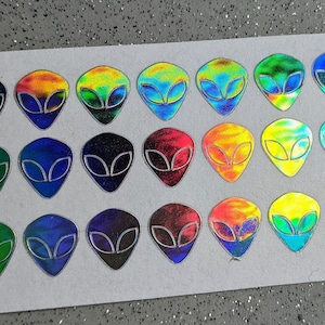 May include: A sheet of holographic stickers featuring alien faces in various colors, including blue, green, red, yellow, and black.