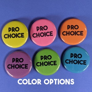 K&ouml;nnte beinhalten: Sechs runde Kn&ouml;pfe mit dem Text "Pro Choice" in schwarzer Schrift auf verschiedenen farbigen Hintergr&uuml;nden. Die Farben sind gelb, rosa, orange, lila, gr&uuml;n und blau. Die Kn&ouml;pfe sind in zwei Reihen zu je drei angeordnet. Der Text "COLOR OPTIONS" befindet sich unter den Kn&ouml;pfen.