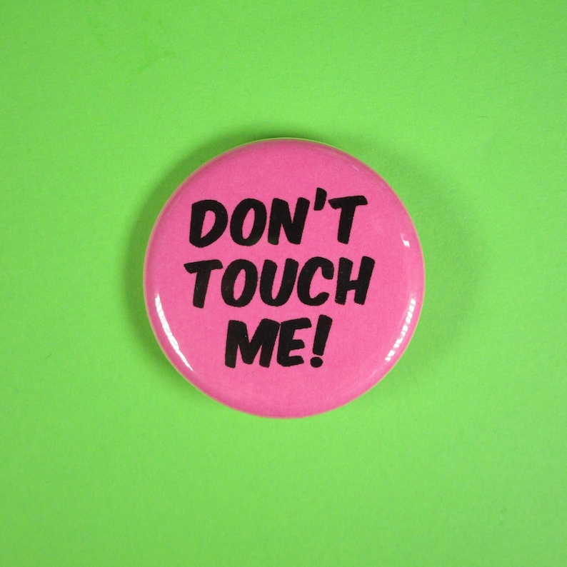 K&ouml;nnte beinhalten: Rosafarbener Knopf mit dem Text "Don't Touch Me!" in schwarzen Buchstaben.