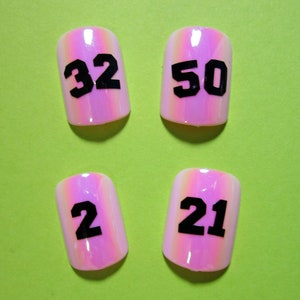 May include: Four pink iridescent fake nails with black numbers 32, 50, 2, and 21 printed on them.