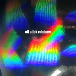 May include: A close-up of iridescent, holographic material with a rainbow oil slick effect. The material has a textured, wavy pattern and reflects light in a variety of colors.