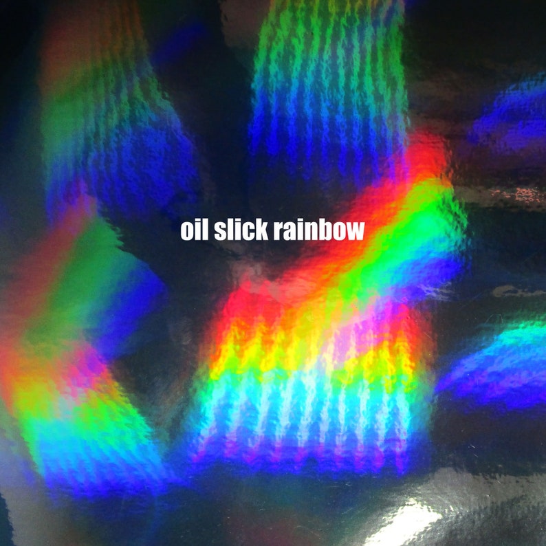 May include: A close-up of iridescent, holographic material with a rainbow oil slick effect. The material has a textured, wavy pattern and reflects light in a variety of colors.