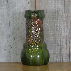 May include: A green ceramic pitcher with a glossy finish. The pitcher features a textured, embossed design in shades of red and brown on the front. The body of the pitcher has vertical ridges, and the overall shape is bulbous at the base.