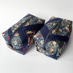 May include: Two rectangular zipped pouches with a floral design in blue, red, and green. Dark blue fabric is used for the zip and corners. These pouches are suitable for cosmetics or small items. Each pouch measures approximately 20cm in length.