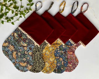 May include: A collection of Christmas stockings with a burgundy velvet top and patterned fabric bottoms. The fabric features floral and bird designs in various colors, with a cream-colored pom-pom trim.