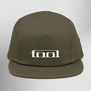 May include: Olive green five-panel cap with a flat brim. The word "TOOL" is embroidered in white block letters on the front. The cap is made of a durable fabric and has a structured design.