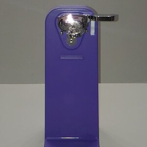 Puede incluir: Un abrelatas manual morado con un mango plateado y un mecanismo de corte plateado.