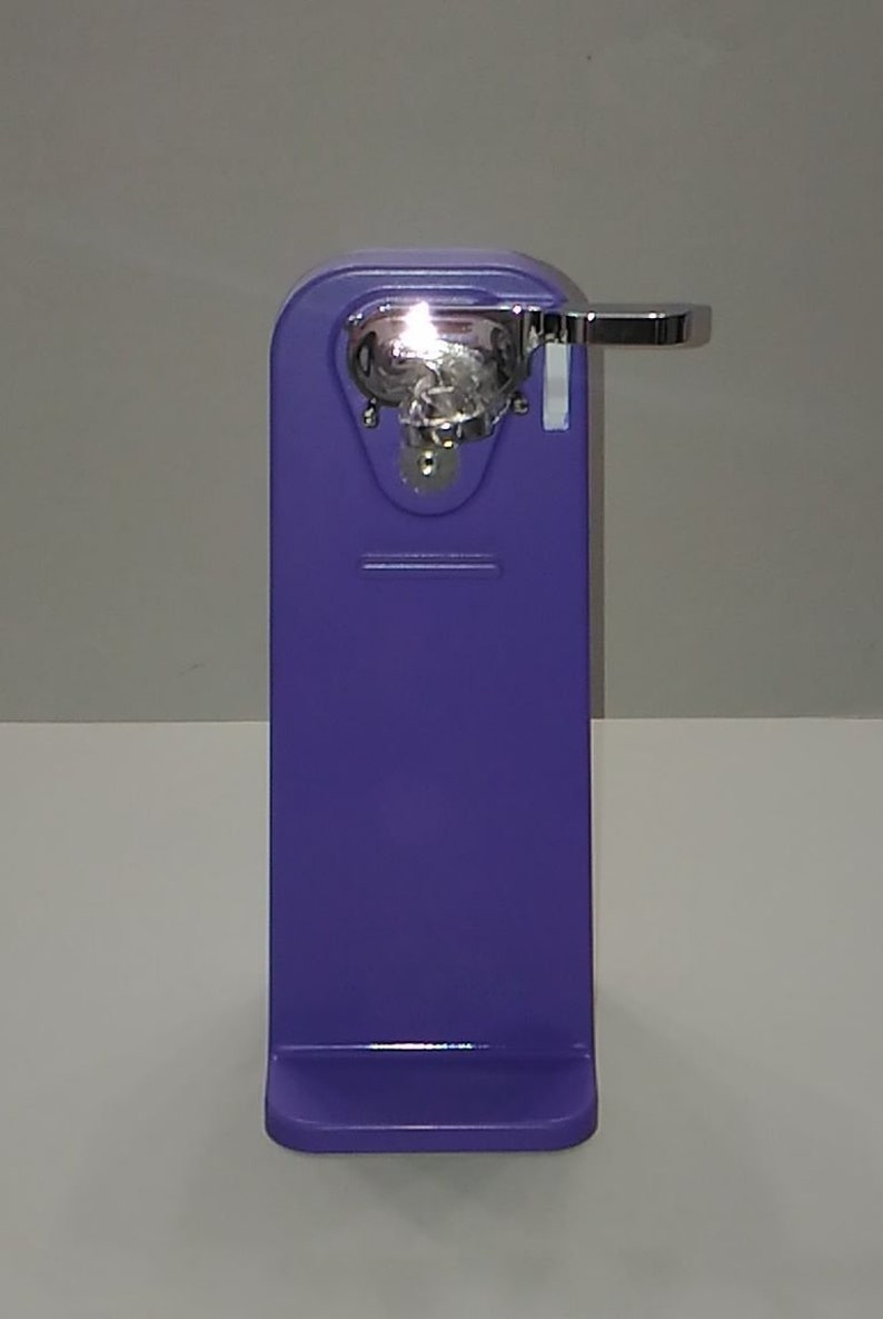 Puede incluir: Un abrelatas manual morado con un mango plateado y un mecanismo de corte plateado.