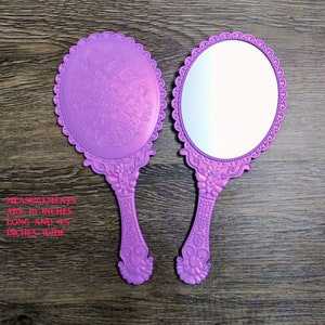 Pode incluir: Dois espelhos de mão roxos com designs ornamentados. Os espelhos medem 25,4 cm de comprimento e 11,4 cm de largura.