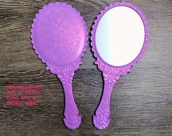 Pode incluir: Dois espelhos de mão roxos com designs ornamentados. Os espelhos medem 25,4 cm de comprimento e 11,4 cm de largura.