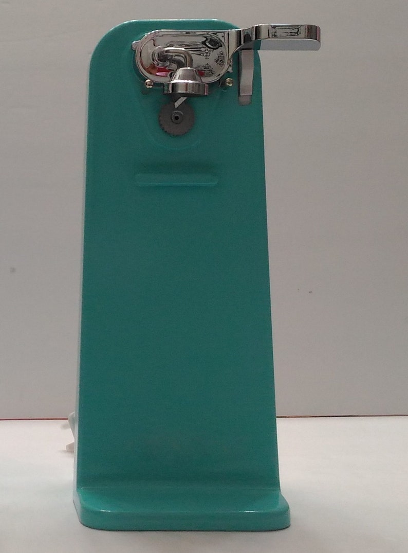 Pode incluir: Um abridor de latas manual azul turquesa com uma pega cromada e uma engrenagem na frente.