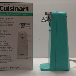 Pode incluir: Um abridor de latas el&eacute;trico turquesa com uma alavanca prateada e uma base branca. A caixa mostra a marca Cuisinart e as caracter&iacute;sticas do abridor de latas. O texto na caixa diz "The Most Trusted Name in the Kitchen" e "Power Cut Series Can Opener".