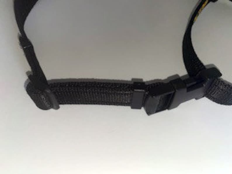 May include: Close-up of a black adjustable strap with a plastic buckle. The strap is made of a woven fabric.
