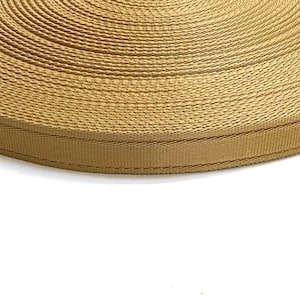 May include: A close-up of a roll of tan webbing. The webbing is woven with a textured pattern and has a subtle sheen.