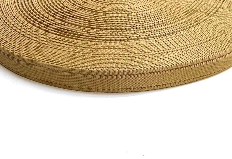 May include: A close-up of a roll of tan webbing. The webbing is woven with a textured pattern and has a subtle sheen.