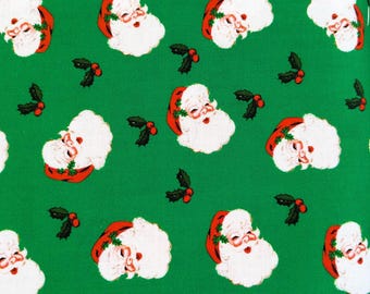 Puede incluir: Una tela verde con un patrón repetido de caras de Papá Noel y ramitas de acebo. Las caras de Papá Noel tienen barbas blancas y gorros rojos. El acebo tiene hojas verdes y bayas rojas. Ideal para manualidades navideñas.