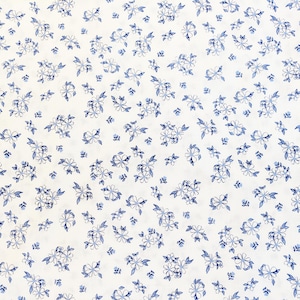 May include: A white fabric featuring a repeating pattern of small, delicate blue flowers and leaves. The floral design is scattered across the surface in a consistent, dense arrangement, showcasing thin, hand-drawn style blue outlines.