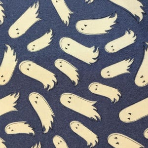 Può includere: Un motivo in tessuto caratterizzato da un design ripetitivo di figure di fantasmi color bianco sporco con semplici occhi neri su uno sfondo blu scuro. I fantasmi sono orientati in varie direzioni, ognuno con una testa arrotondata e una coda.