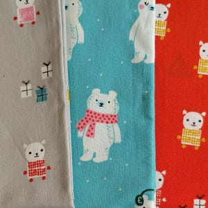 Può includere: Tre campioni di tessuto con motivi ripetuti di orsi polari e regali. Il primo campione è grigio con scatole regalo bianche e rosse e un orso polare con una sciarpa rossa e bianca. Il secondo campione è blu con orsi polari bianchi e una sciarpa rossa e bianca. Il terzo campione è rosso con scatole regalo gialle e orsi polari bianchi.