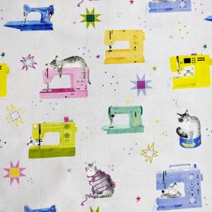 May include: White fabric featuring a repeating pattern of sewing machines and cats. The sewing machines are in blue, yellow, pink, and green. The cats are grey and white. The design also includes star and dot accents.