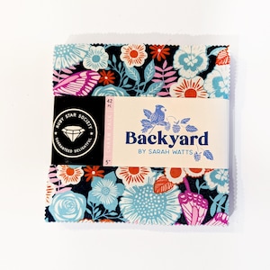 Op de afbeelding: Een vierkante stapel van 42 stoffen vierkantjes, bekend als een charm pack, met een donkerblauwe achtergrond en een bloemen- en vlinderpatroon in lichtblauw, oranje en roze. Een witte papieren band toont de tekst Backyard by Sarah Watts.