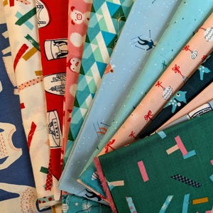 Op de afbeelding: Een verzameling gevouwen stofstalen met diverse patronen, waaronder een blauwe achtergrond met witte contouren, rood met Parijse bezienswaardigheden, roze met varkensgezichten, geometrische turquoise driehoeken en lichtblauw met skiërs.