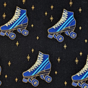 May include: A repeating pattern featuring blue roller skates with gold detailing on a black background. The skates have light blue stripes and white laces. Gold starbursts are scattered across the design.