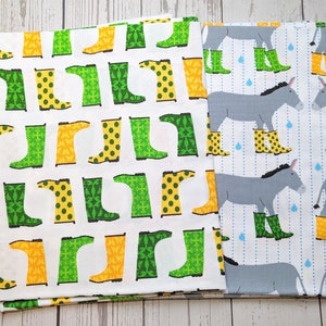 May include: Two fabric panels, one with a white background and a repeating pattern of green, yellow, and white rain boots, and the other with a blue and white striped background and a repeating pattern of gray donkeys wearing yellow rain boots.