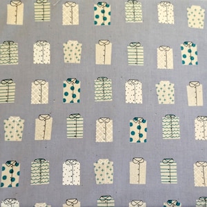 Peut inclure: Un motif répétitif sur tissu représentant des chemises boutonnées stylisées. Les chemises sont de couleurs variées, dont blanc, turquoise et beige, avec des motifs à pois, rayures et croix. Le fond est bleu clair.