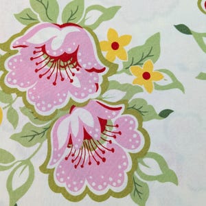 May include: A white fabric featuring a repeating floral pattern with large pink flowers, small yellow blossoms, and green leaves. The pink flowers have white scalloped edges, red centers, and thin red stamens, while the green leaves have dark outlines.