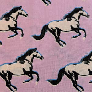 Puede incluir: Un patrón repetido de caballos corriendo sobre un fondo rosa. Los caballos están representados en blanco y negro con detalles azules, creando un diseño dinámico y artístico. Ideal para proyectos de costura y manualidades.