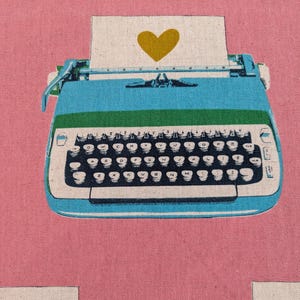 May include: A vintage blue typewriter with a green carriage return and a white paper with a yellow heart on it. The typewriter has a black keyboard with white keys.