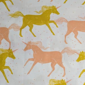 May include: White fabric with a repeating pattern of yellow and peach-colored unicorns. The unicorns are depicted in a running pose with flowing manes and tails. Small peach dots are scattered across the white background.