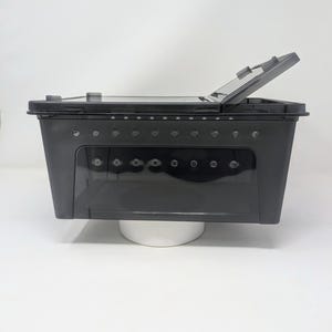 May include: Black plastic storage container with a clear lid and ventilation holes. The lid is open and the container is sitting on a white surface.