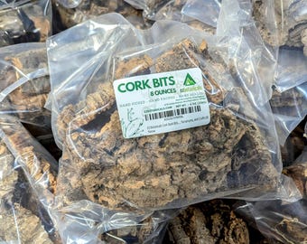 May include: A clear plastic bag filled with brown cork bits. The bag has a label that reads "Cork Bits 8 Ounces" and "ezbotanicals". The label also includes the website address "ezbotanicals.com" and the net weight "8 oz (226g)".
